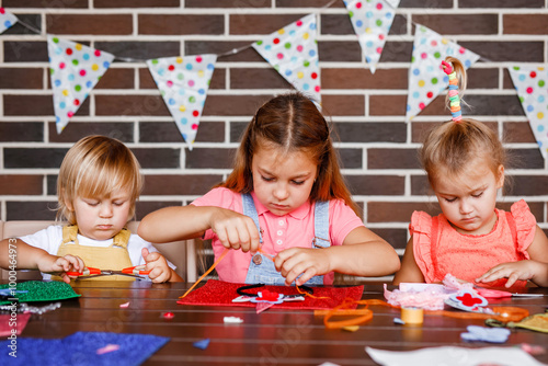 A little toddler boy and two girls cutting something out of beautiful paper at a party