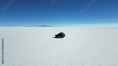 Drone shot flying away from a car in the center of the Uyuni salt flat, the largest in the world, in Bolivia with mountains visible on the far horizon