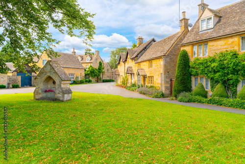 Fototapeta Naklejka Na Ścianę i Meble -  A small park with an old well landmark in a picturesque street of stone cottages in the Cotswold village of Lower Slaughter, England.