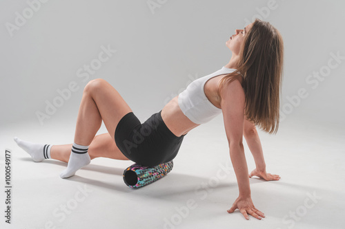 Caucasian woman doing roller exercise for myofascial release on white background. Self-massage of thighs.  photo