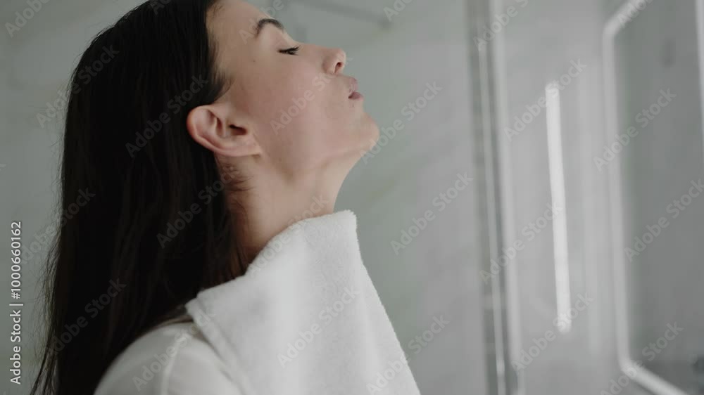 Young woman drying her face with a white towel in a bathroom. She appears relaxed after completing her skincare routine. Woman Drying Face With Towel in Bathroom After Skincare Routine
