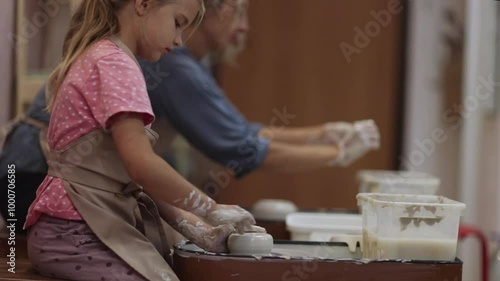 mother and child daughter moulding together from clay on pottery wheel  a pottery class.
