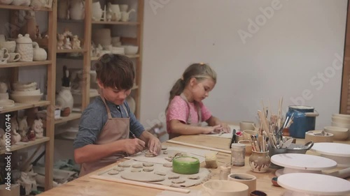 kids works with clay makes  ceramic plate in pottery school.  Children arts a crafts class in workshop.  the child sculpts from clay.