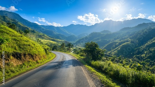 Winding road through lush green mountains under bright blue sky and sun