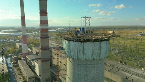 Construction site of a power plant a high chimney.Dangerous work at height.A renovation is smokestack.Contractor repairing a chimney at a highrise.Workers in a hard hat.Dangerous work at the daytime.