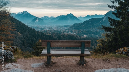 A blank wooden bench at a scenic lookout, overlooking mountains and a valley filled with trees.