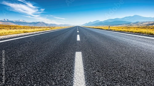 A smooth asphalt highway stretching into the distance under a clear blue sky, with mountains visible on the horizon.