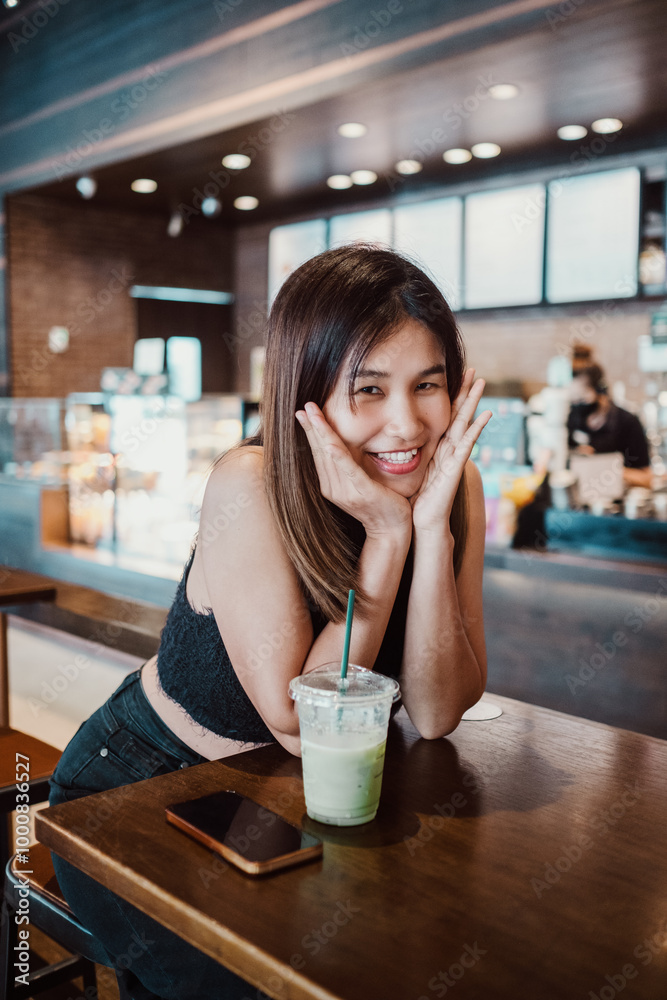 Smiling young woman sitting at a cafe table with a refreshing drink, enjoying the cozy and modern ambiance. Smiling young woman sitting at a cafe table with a refreshing drink, enjoying the cozy and modern ambiance.
