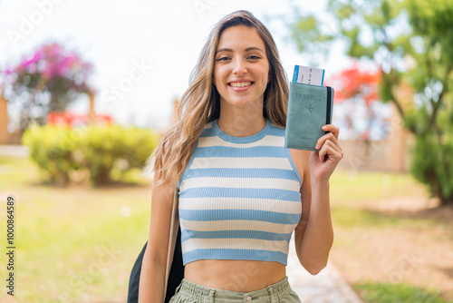 Young pretty woman holding a passport at outdoors smiling a lot