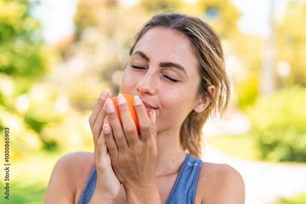 Young blonde woman at outdoors holding an orange Young blonde woman at outdoors holding an orange
