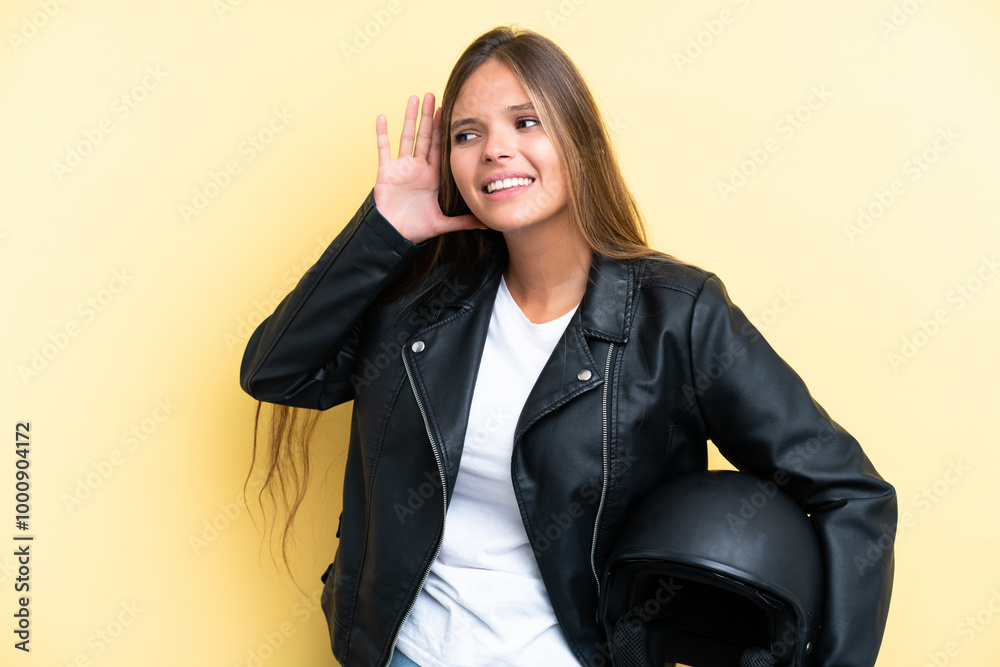 Young caucasian woman with a motorcycle helmet isolated on yellow background listening to something by putting hand on the ear Young caucasian woman with a motorcycle helmet isolated on yellow background listening to something by putting hand on the ear