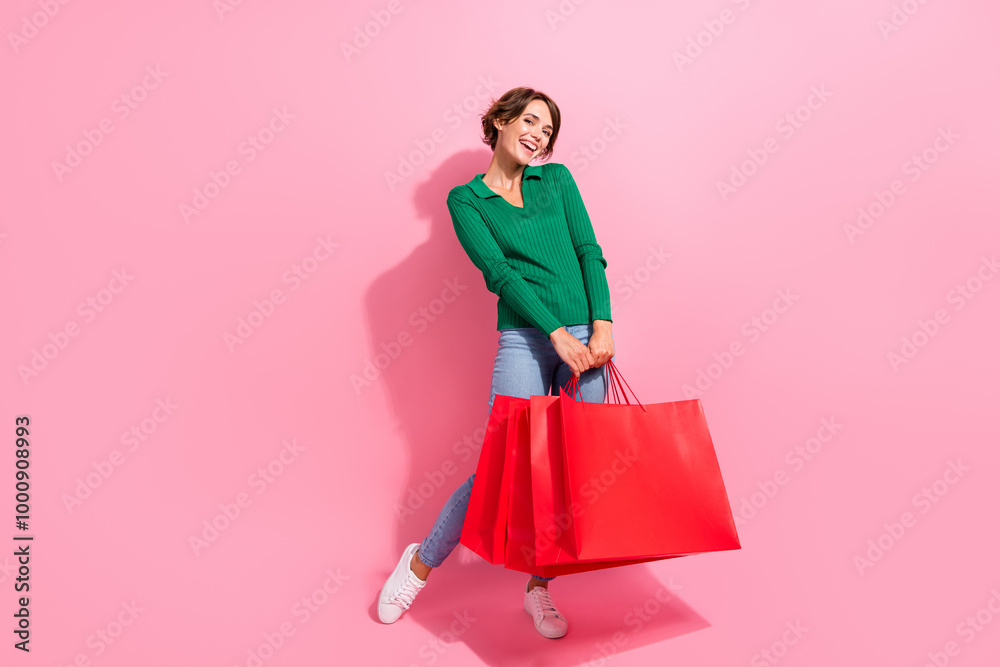 Full length photo of nice pretty young woman posing holding red packages cute model shopaholic glad isolated on pink color background Full length photo of nice pretty young woman posing holding red packages cute model shopaholic glad isolated on pink color background