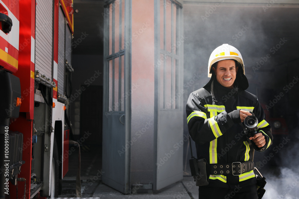 Obraz premium Portrait of firefighter in uniform with high pressure water jet near fire truck outdoors