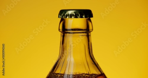 A beer bottle with a methly cap rotates on a yellow background