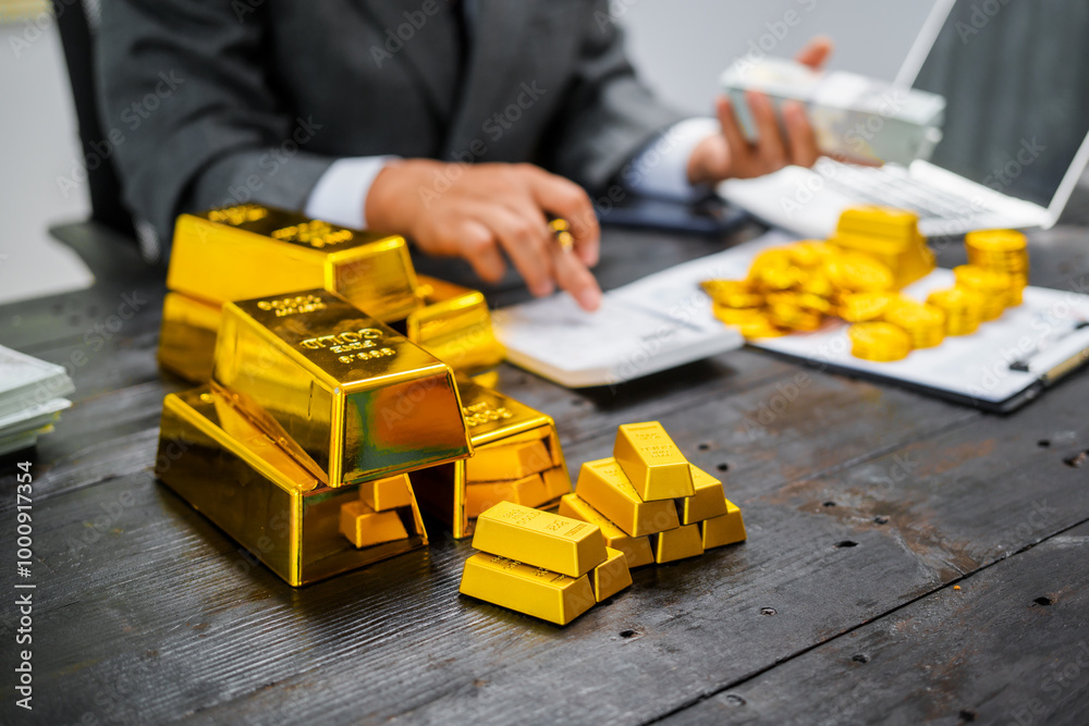 Obraz premium Businessman in suit sits at his desk, holding a shining gold bar. financial charts, the scene symbolizes wealth, investment success, growing influence of cryptocurrency and blockchain.