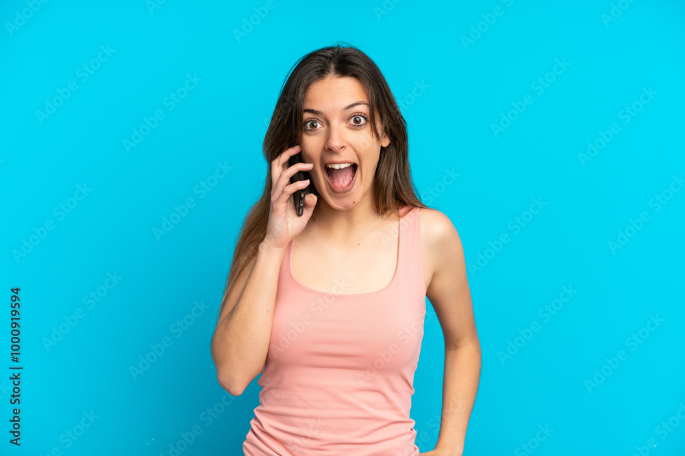 Fototapeta premium Young caucasian woman using mobile phone isolated on blue background with surprise facial expression