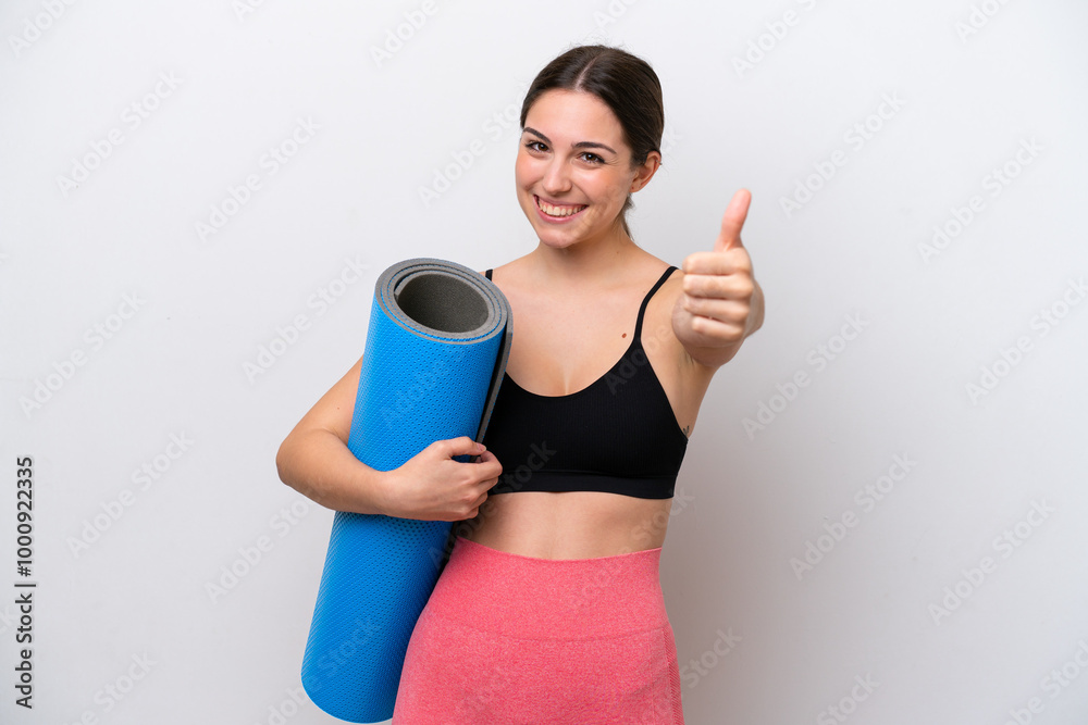 Young sport girl going to yoga classes while holding a mat isolated on white background with thumbs up because something good has happened Young sport girl going to yoga classes while holding a mat isolated on white background with thumbs up because something good has happened
