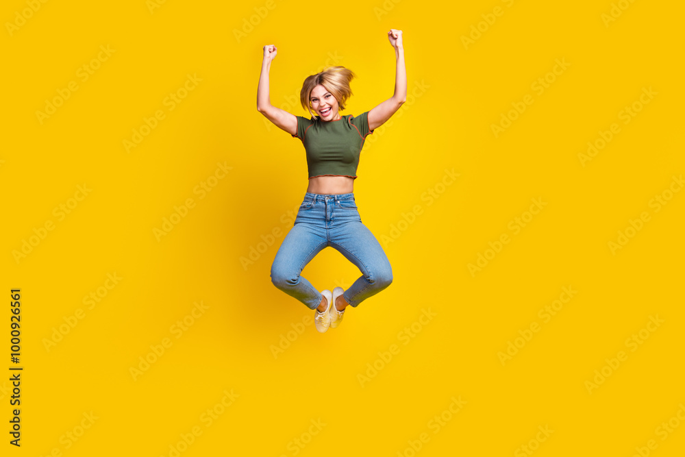 Full size photo of overjoyed girl dressed khaki crop top jeans jump raising fists up win gambling isolated on yellow color background Full size photo of overjoyed girl dressed khaki crop top jeans jump raising fists up win gambling isolated on yellow color background