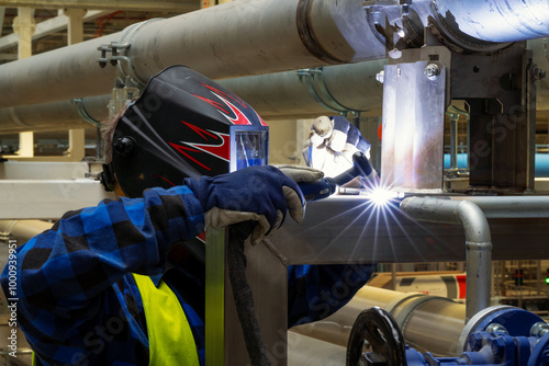Welder welding steel elements with TIG MIG method indoors in protective equipment in industrial setting