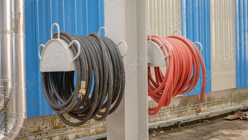 Hoses Wrapped Around Metal Stands. Two hoses, one black and one red, are neatly coiled around metal stands attached to a wall.