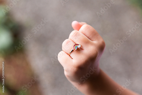 Close up photo of a hand with a rainbow ring worn around the finger photo