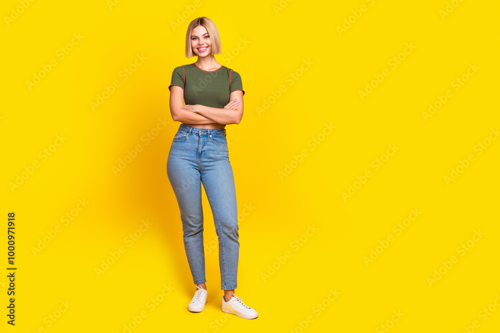 Full length photo of positive nice girl dressed khaki t-shirt arms folded near logo empty space isolated on yellow color background Full length photo of positive nice girl dressed khaki t-shirt arms folded near logo empty space isolated on yellow color background