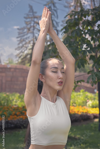 Young Asian woman practicing yoga in the park. Girl meditating in nature. Healthy lifestyle. Concept of vitality, calmness, relaxation, mindfulness, zen energy.