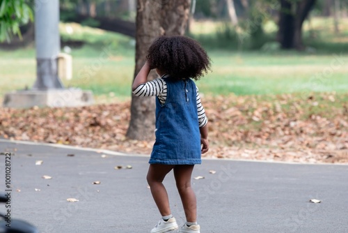 Adorable young African-American girl Afro curly hair walking on park path appears to be exploring her surroundings, capturing the essence of curiosity and innocence, holiday, summertime, carefree