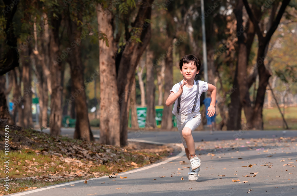 Fototapeta premium Young Asian boy running energetically down a tree-lined path in a park, capturing a playful and active moment outdoors. carefree expression reflects excitement and freedom to enjoy fresh air outdoor