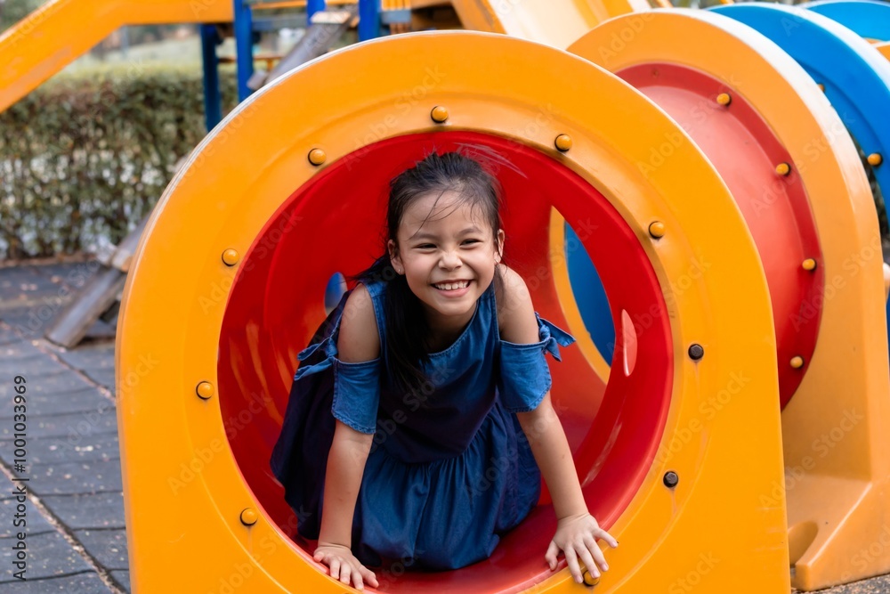 Young Asian elementary schoolgirl crawling through a colorful tunnel on a playground. weekend carefree holiday in park. bright playground equipment and focus expression capture childhood exploration Young Asian elementary schoolgirl crawling through a colorful tunnel on a playground. weekend carefree holiday in park. bright playground equipment and focus expression capture childhood exploration