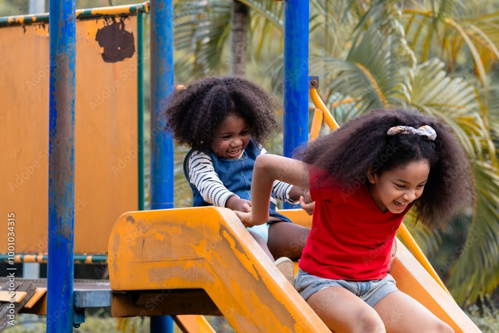 Two African American sibling girls joyful and laughing sliding down a yellow playground together, having fun in summertime holiday, the moment captures outdoor activities weekend children in park Two African American sibling girls joyful and laughing sliding down a yellow playground together, having fun in summertime holiday, the moment captures outdoor activities weekend children in park