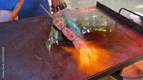 Asian street food vendor selling grilled squid. An adult man grilling squid skewers with blow torch fire