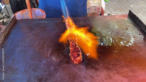 Asian street food vendor selling grilled squid. An adult man grilling squid skewers with blow torch fire