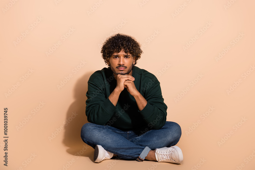 Full size photo of nice young man sit floor wear sweater isolated on beige color background Full size photo of nice young man sit floor wear sweater isolated on beige color background