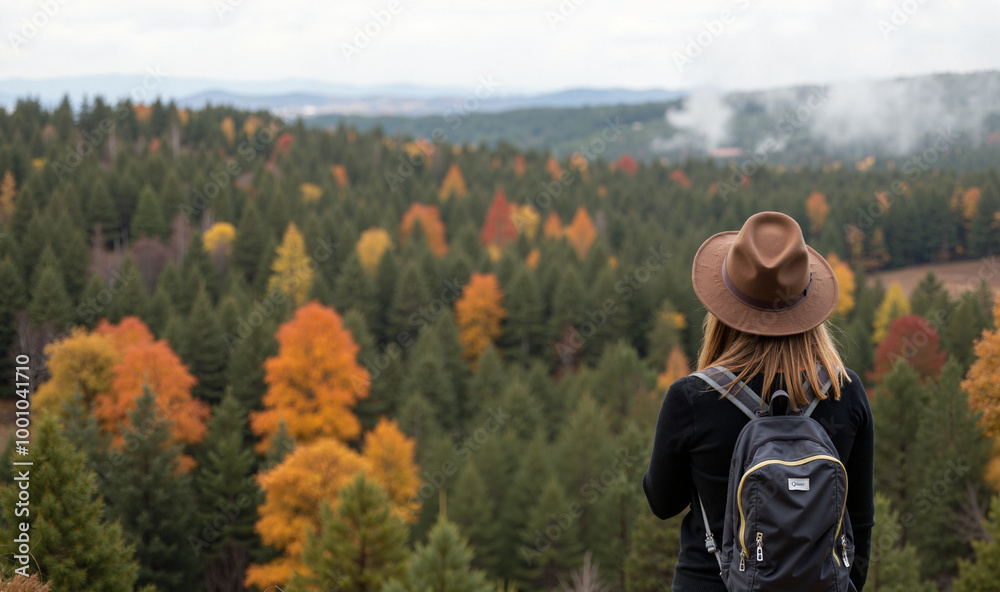 A woman with long, blonde hair, wearing a brown fedora hat, a black sweater, and a gray backpack, stands with her back to the camera, looking out at a breathtaking autumnal forest landscape. The fores A woman with long, blonde hair, wearing a brown fedora hat, a black sweater, and a gray backpack, stands with her back to the camera, looking out at a breathtaking autumnal forest landscape. The fores