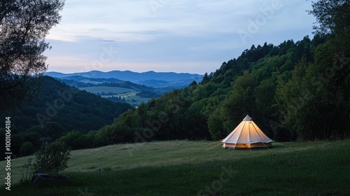 A tent nestled at the edge of a forest clearing, with rolling hills and distant mountains in the background, illuminated by soft evening light.