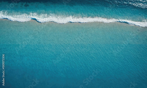 An aerial view of the ocean with a white wave breaking near the shore