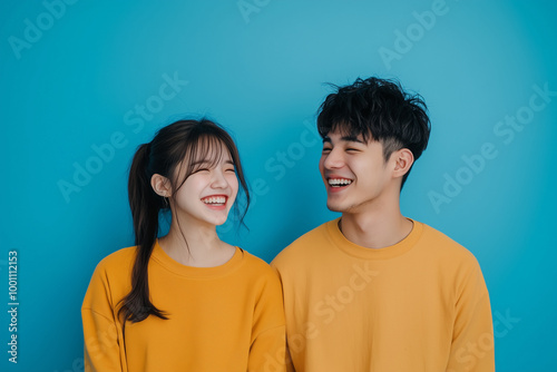 A young Asian couple dressed in casual everyday wear, caught in a moment of shared laughter happy lovebird on the solid background 