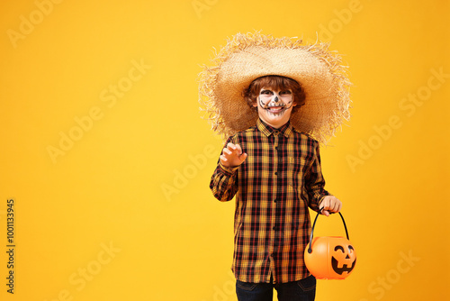 Funny boy with pumpkin bucket dressed like scarecrow on yellow background, space for text. Halloween celebration