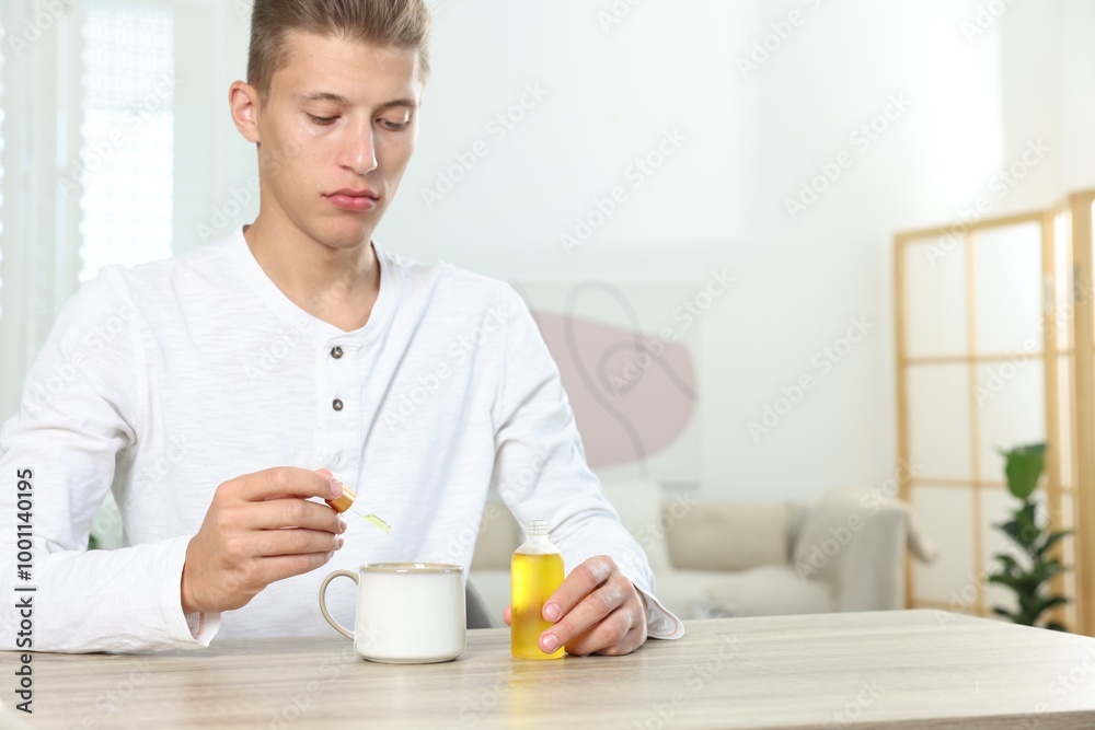 Young man dripping CBD tincture into drink at wooden table, space for text Young man dripping CBD tincture into drink at wooden table, space for text