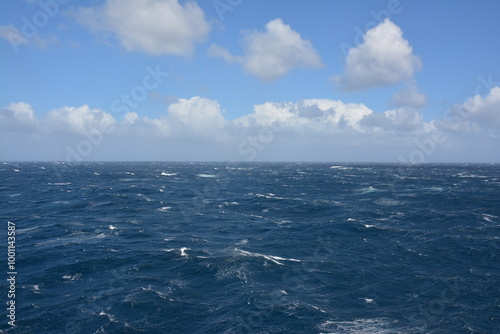 Foto A dynamic view of the ocean with strong waves and choppy waters under a partly cloudy blue sky, showing the intensity of open sea conditions