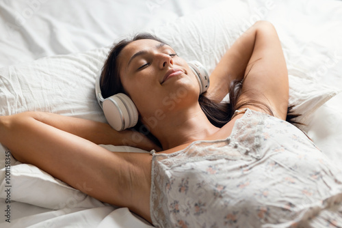 Beautiful young woman listening to music with headphones while relaxing lying on the bed at home photo