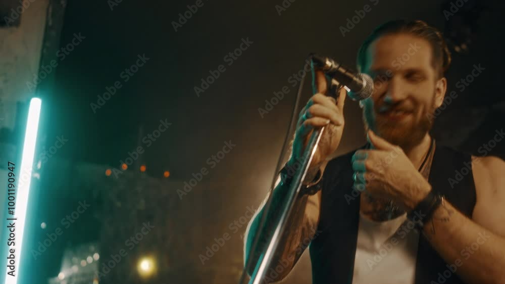 Medium close-up of young Caucasian male vocalist standing on stage holding microphone and singing with enjoyment and passion Medium close-up of young Caucasian male vocalist standing on stage holding microphone and singing with enjoyment and passion