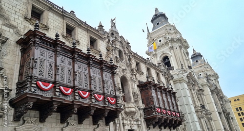 Historical building with intricate architectural designs. Features balconies with elaborate wooden balustrades and red and white banners.  