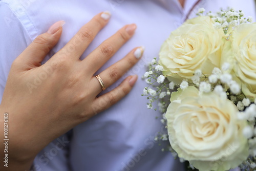 A bride’s hand gently rests on the groom’s shoulder, highlighting her elegant wedding ring and the delicate bridal bouquet in the background