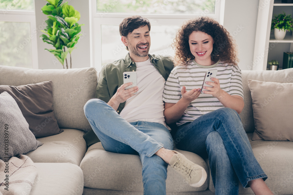 Photo of two young people sit couch show smart phone modern interior apartment indoors Photo of two young people sit couch show smart phone modern interior apartment indoors