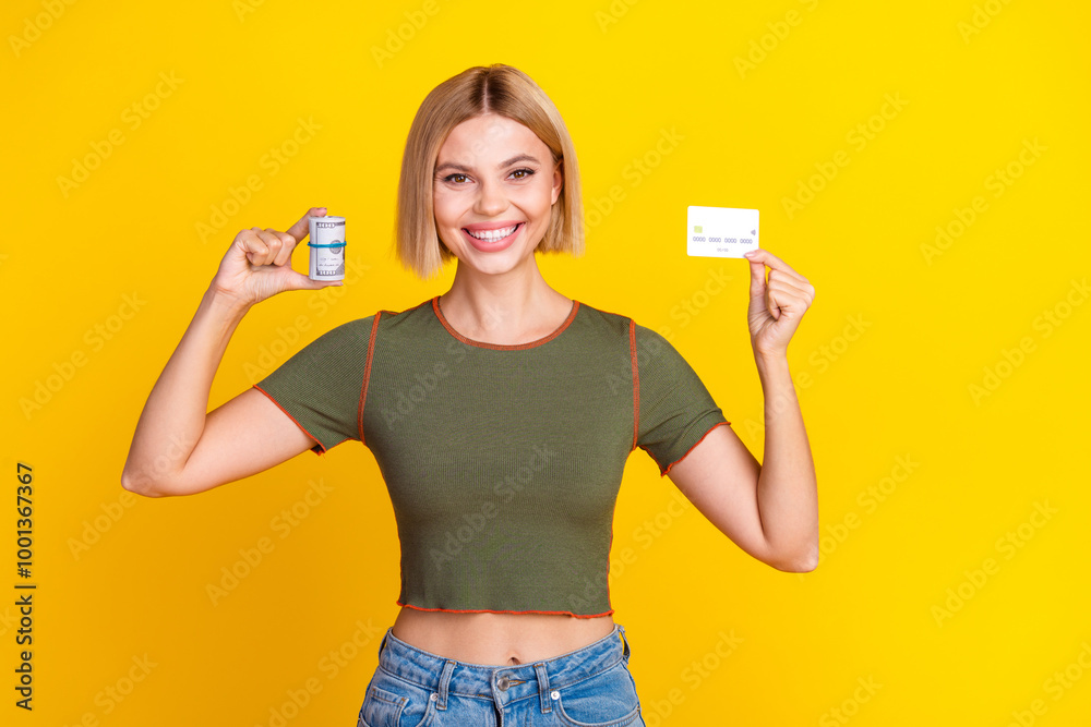 Photo of positive good mood girl with bob hairdo dressed khaki crop top holding credit card dollars isolated on yellow color background Photo of positive good mood girl with bob hairdo dressed khaki crop top holding credit card dollars isolated on yellow color background