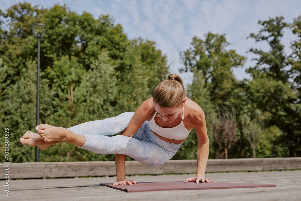 Toned and strong woman testing advanced yoga pose called eight angle on mat unde open sky in park