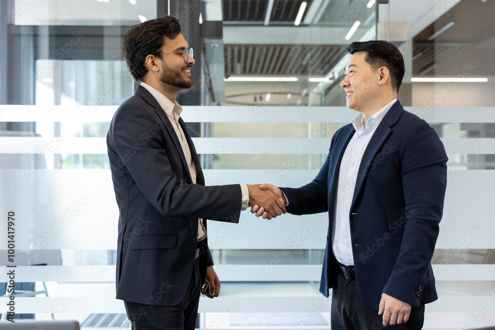 Two businessmen exchange a confident handshake in modern office environment, showcasing professional interaction and teamwork. They stand facing each other, wearing formal attire Two businessmen exchange a confident handshake in modern office environment, showcasing professional interaction and teamwork. They stand facing each other, wearing formal attire