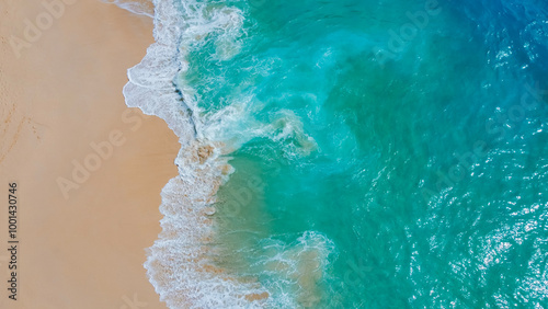 An aerial shot of vibrant turquoise waves meeting the sandy shore, capturing the dynamic motion of the ocean and the tranquil beauty of the untouched beach from above.

